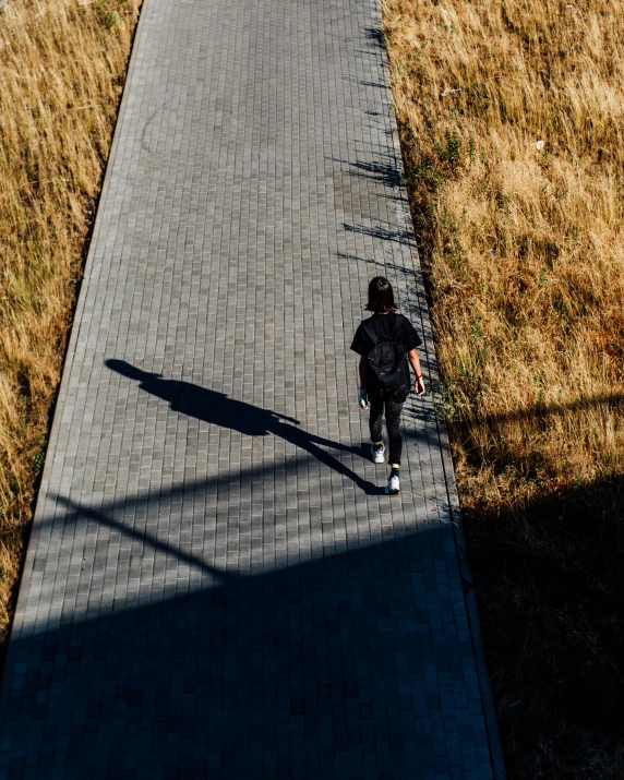 a person riding a skateboard down a sidewalk, by Sebastian Spreng, unsplash contest winner, strong shadow, walking on grass, on an empty stage from above, non-binary