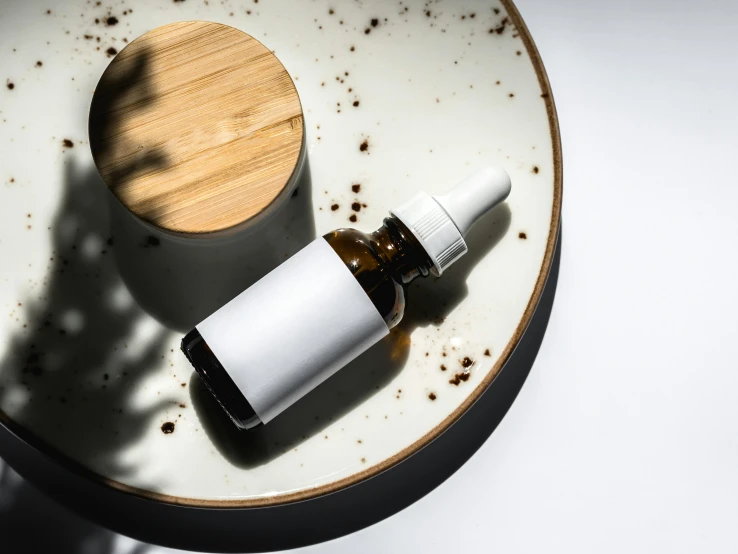 a bottle of essential oil sitting on a plate, inspired by Lubin Baugin, unsplash, made of high tech materials, white clay, brown resin, skincare