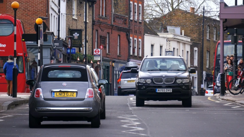 a couple of cars driving down a street next to a red double decker bus, esher, traffic signs, busy small town street, image