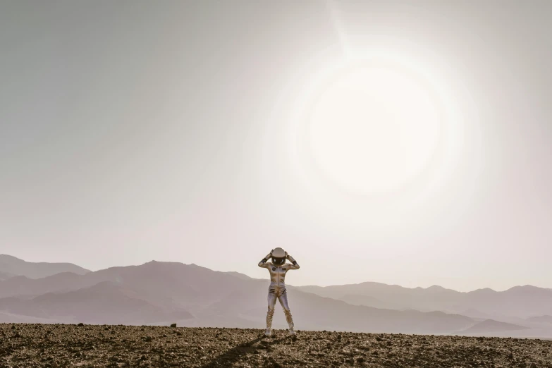 a person standing on top of a dirt field, unsplash contest winner, afrofuturism, blinding sun, mars vacation photo, silver space suit, full body photograph