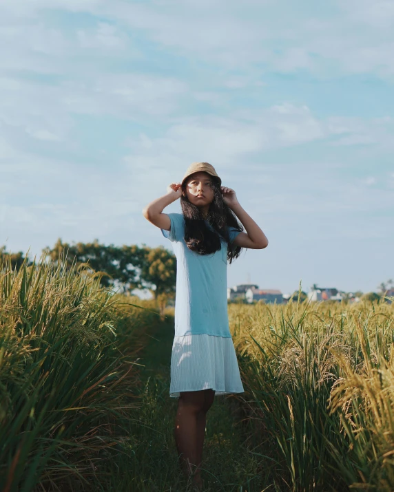 a woman standing in a field of tall grass, inspired by Tan Ting-pho, unsplash, wearing a light blue shirt, wearing a white bathing cap, wearing a dress, set on singaporean aesthetic
