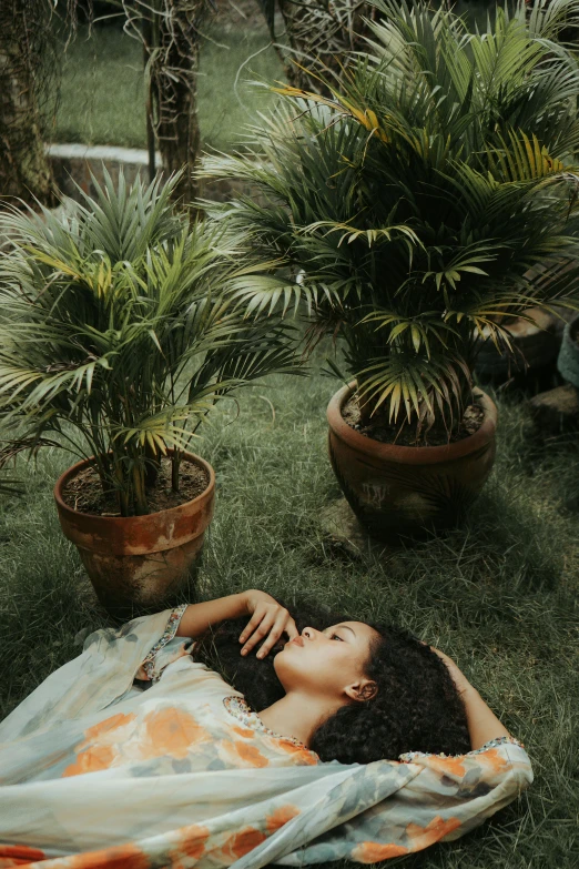 a woman laying on top of a lush green field, inspired by Elsa Bleda, pexels contest winner, renaissance, with interior potted palm trees, natural complexion, dreaming of kissing a girl, tropical houseplants