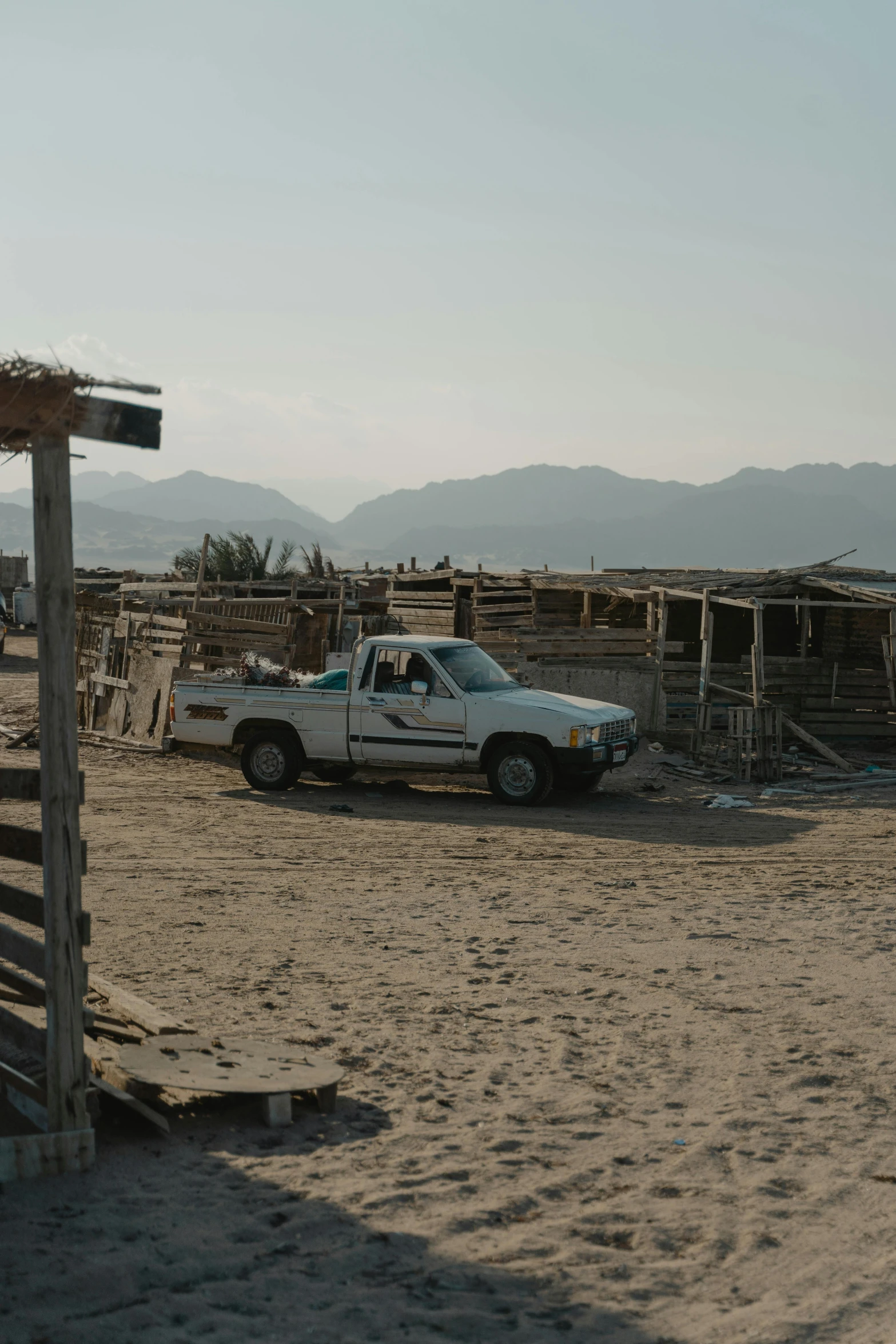 a truck that is sitting in the sand, huts, in the middle of a small colony, 8 k film still, red sea