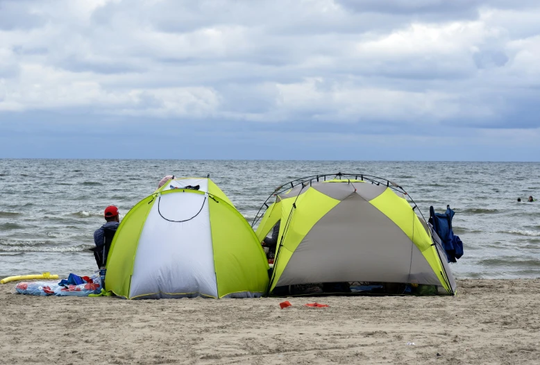 a couple of tents sitting on top of a sandy beach, a photo, by Adam Marczyński, shutterstock, a green, profile image, beach pic, gray