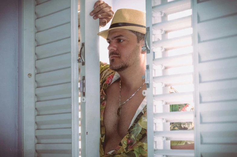 a man wearing a hat looking out of a window, a colorized photo, pexels contest winner, beefcake pose, tropical vibe, exiting from a wardrobe, avatar image