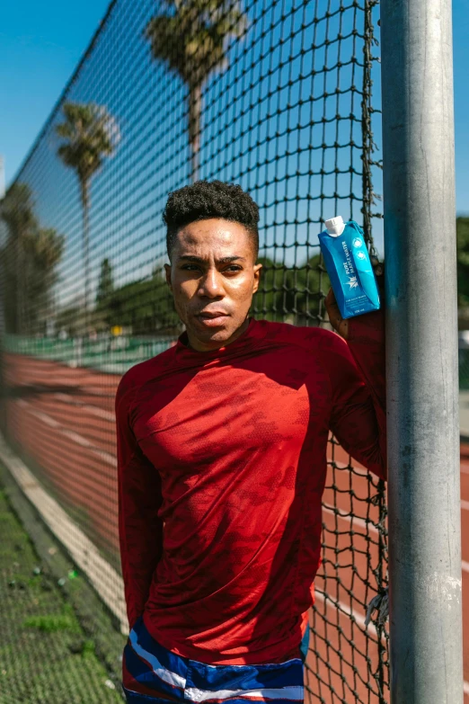 a man leaning against a fence holding a bottle of water, athlete photography, ashteroth, promo image, flattened