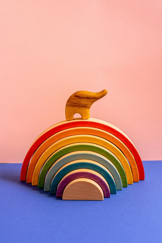 a wooden toy sitting on top of a blue table, by Rachel Reckitt, trending on unsplash, botanical rainbow backdrop, animal - shaped statue, arcs, on textured base; store website