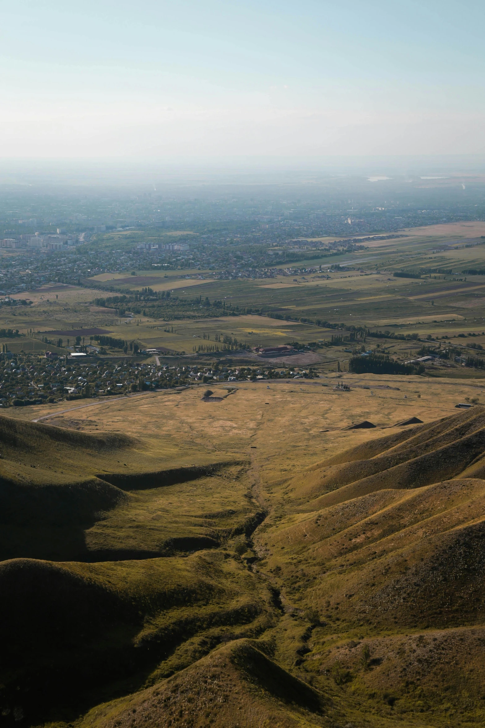 a view of a valley from the top of a hill, by Muggur, land art, grass field surrounding the city, steppe, brown, uv