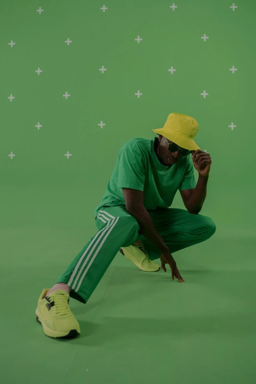 a man sitting on the ground in front of a green screen, an album cover, trending on pexels, visual art, wearing adidas clothing, character with a hat, green and yellow, shades of green