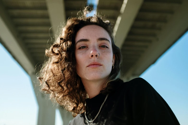 a close up of a person near a bridge, an album cover, by Winona Nelson, unsplash contest winner, photorealism, no makeup wavy hair, androgynous person, lorde, calm face