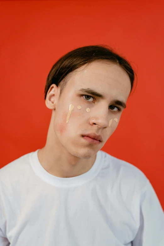 a young man standing in front of a red wall, trending on pexels, hyperrealism, cream dripping on face, sideburns, on a pale background, black eyes and large forehead