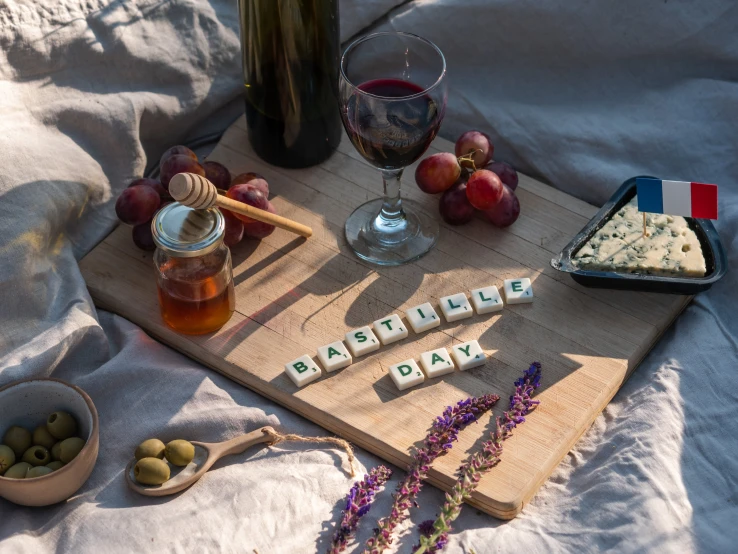 a wooden cutting board sitting on top of a bed next to a bottle of wine, a still life, unsplash, letterism, people on a picnic, purple themed, raf grassetti, cubes on table