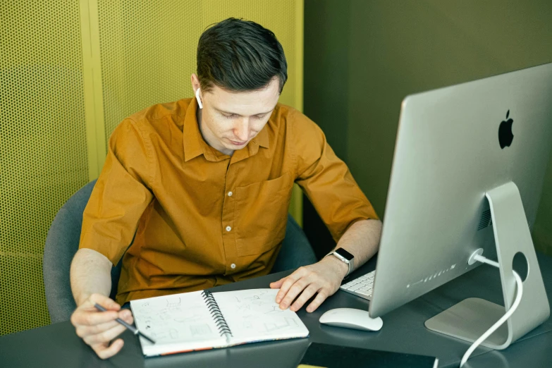 a man sitting at a desk in front of a computer, pexels contest winner, lachlan bailey, holding notebook, profile image, brown