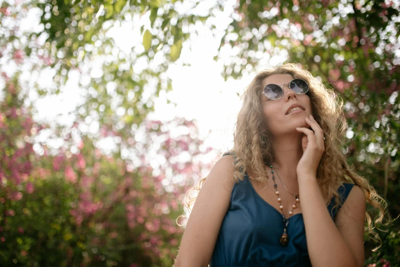 a woman in a blue dress talking on a cell phone, unsplash, wearing shades, young woman looking up, lush surroundings, avatar image