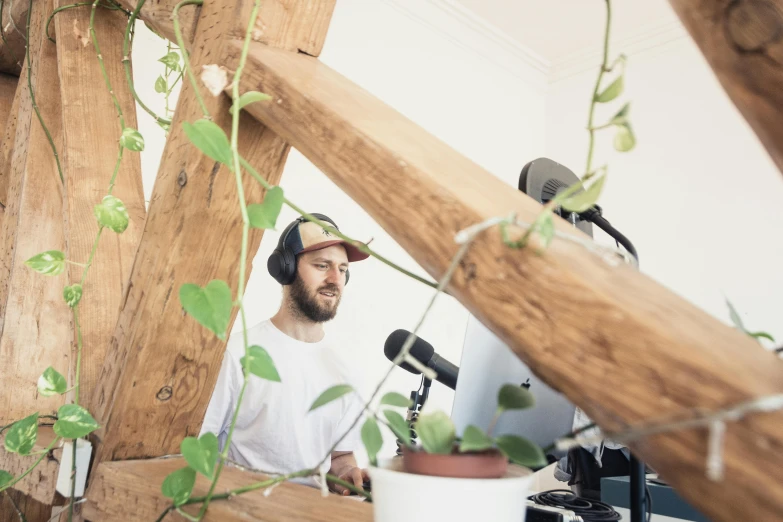 a man that is sitting in front of a microphone, by Matthias Stom, unsplash, filled with plants, wooden headphones, avatar image, low quality footage