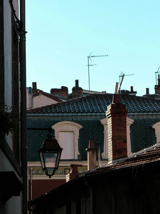 a couple of buildings that are next to each other, a photo, inspired by Jean Tabaud, cloisonnism, roofs, streetlamp, barely visible from the shadows, looking across the shoulder