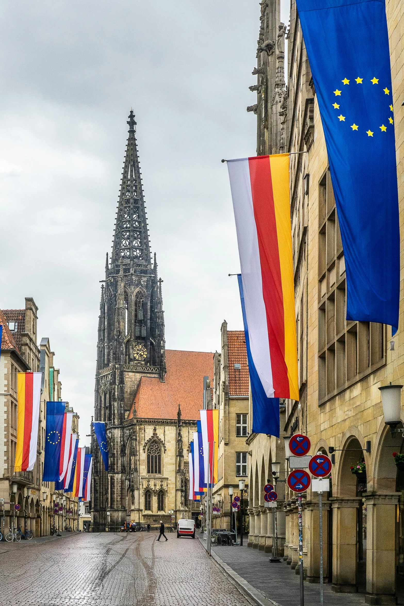 a street filled with lots of flags next to tall buildings, by Juergen von Huendeberg, renaissance, gothic cathedral, lower saxony, yellow and blue ribbons, slide show