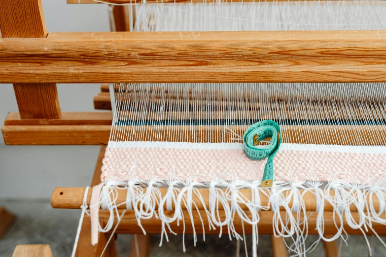 a close up of a weaving machine on a table, inspired by Anni Albers, trending on pexels, arts and crafts movement, pink white turquoise, wooden jewerly, white scarf, stranding straight