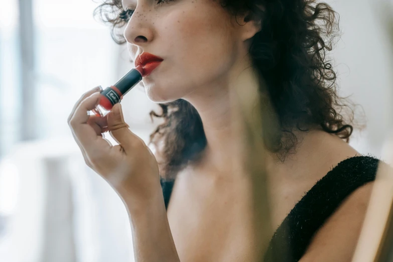 a woman putting on lipstick in front of a mirror, inspired by Nan Goldin, pexels contest winner, red and black details, portrait emily ratajkowski, curly haired, red - black