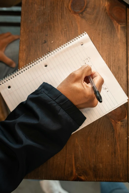 a person sitting at a table writing on a notebook, top down shot, 2019 trending photo, thumbnail, academic clothing