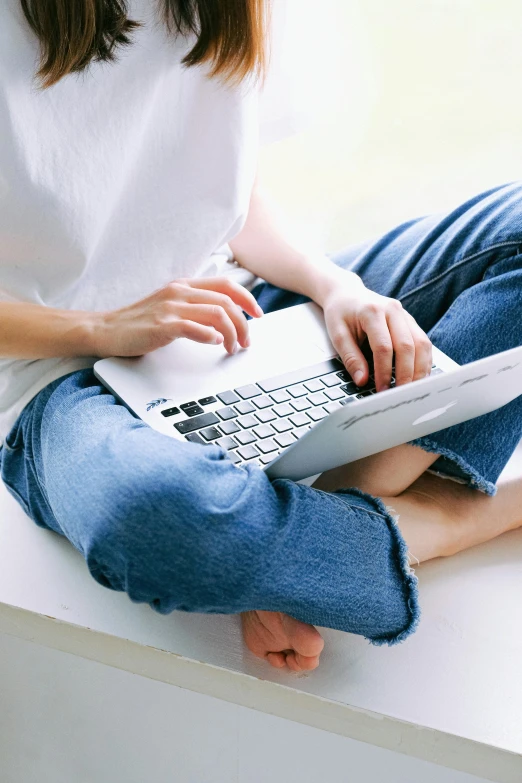 a woman sitting on a window sill using a laptop, pexels, white shirt and blue jeans, early 2 0 0 0 s, on a couch, zoomed in