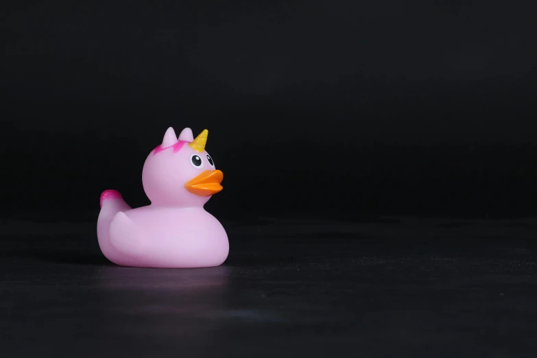 a pink rubber duck with a crown on its head, unsplash, minimalism, black background, shot on sony a 7 iii, toy, relaxing