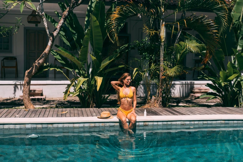 a woman sitting on the edge of a swimming pool, pexels contest winner, next to a tropical pool, in a yellow bikini, 🦩🪐🐞👩🏻🦳, dreampool rooms