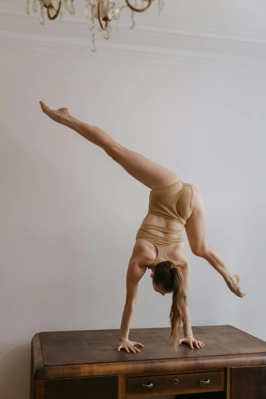 a woman doing a handstand on top of a wooden table, by Jessie Algie, arabesque, ochre, low quality photo, lachlan bailey, athletic body