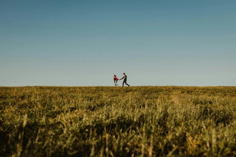 a couple walking across a field holding hands, by Peter Churcher, unsplash contest winner, on a hill, childish, prairie, chasing a kangaroo