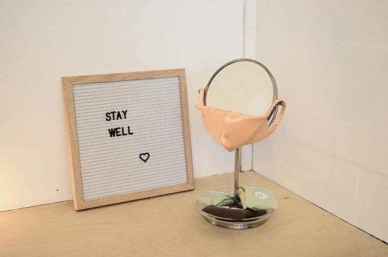 a mirror sitting on top of a table next to a letter board, a still life, by Sylvia Wishart, unsplash, new sculpture, surgical mask covering mouth, beige, peach and goma style, shelf