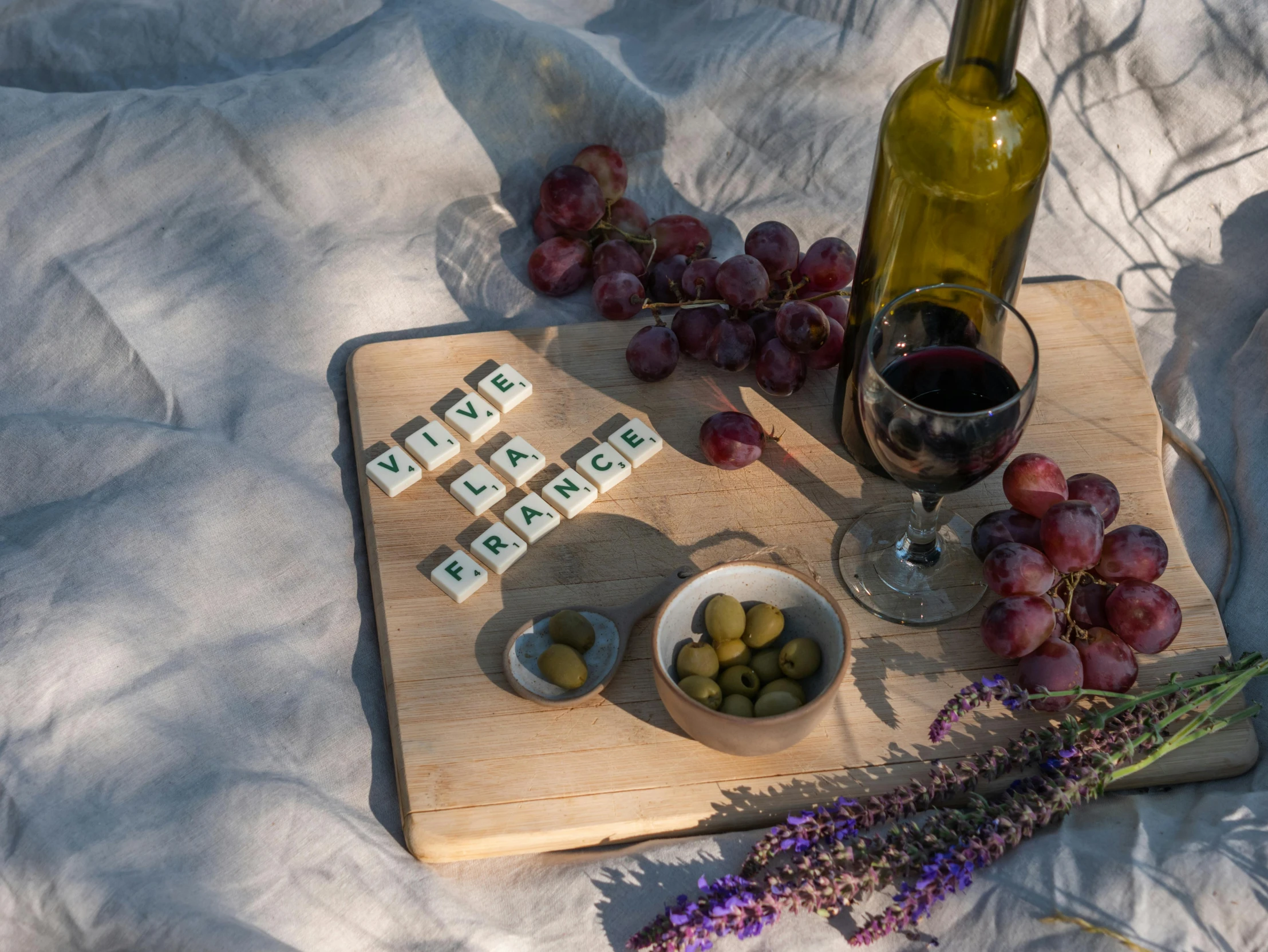 a wooden cutting board topped with grapes next to a bottle of wine, inspired by Louis Stettner, pexels contest winner, statue of a cubes and rings, having a picnic, game board, a wooden