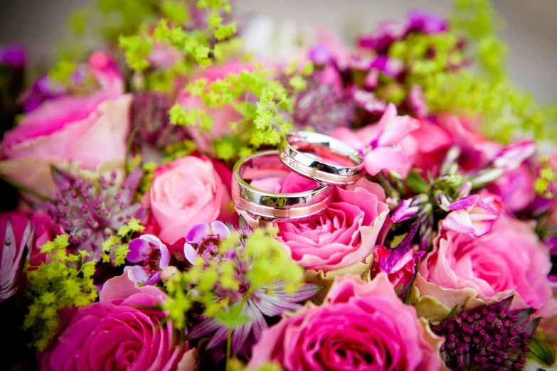 two wedding rings sitting on top of a bouquet of flowers, by Julian Allen, pexels, vibrant pink, platinum jewellery, carefully crafted, highly polished
