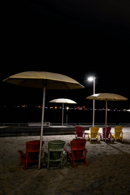 a group of umbrellas sitting on top of a sandy beach, at night, chairs, harsh flash photo at night, harbor