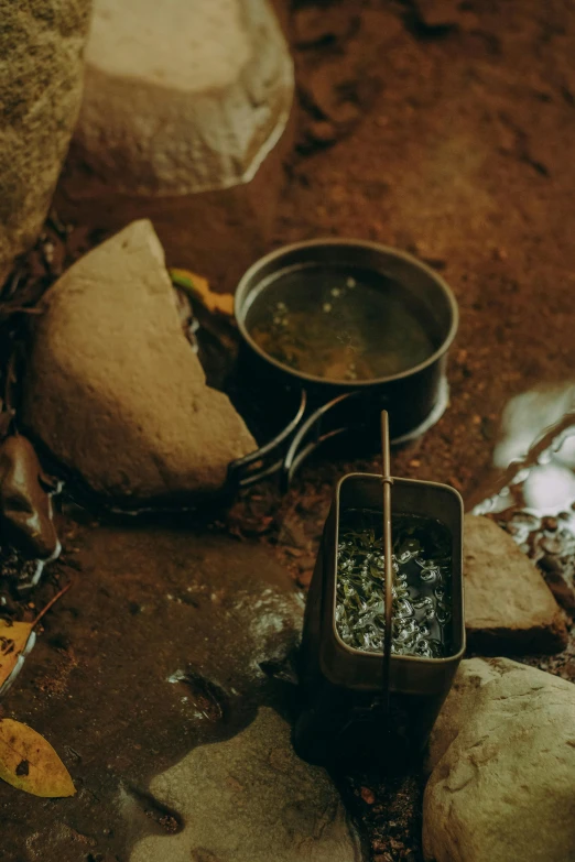 a couple of pots that are on some rocks, a still life, by Elsa Bleda, unsplash, tins of food on the floor, small stream, boiling, high angle close up shot