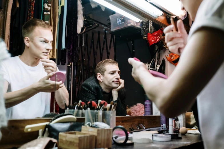 a man brushing his teeth in front of a mirror, a portrait, by Joe Bowler, unsplash, fantastic realism, 3 actors on stage, huge earrings and queer make up, putting makeup on, lachlan bailey