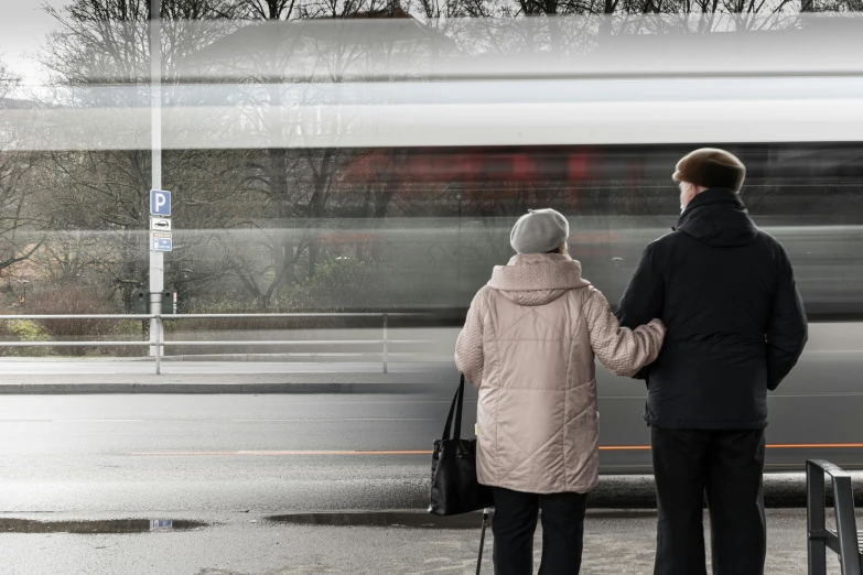 a man and a woman standing in front of a train, by Adam Marczyński, pexels contest winner, realism, bus stop, dementia, seen from the back, older woman