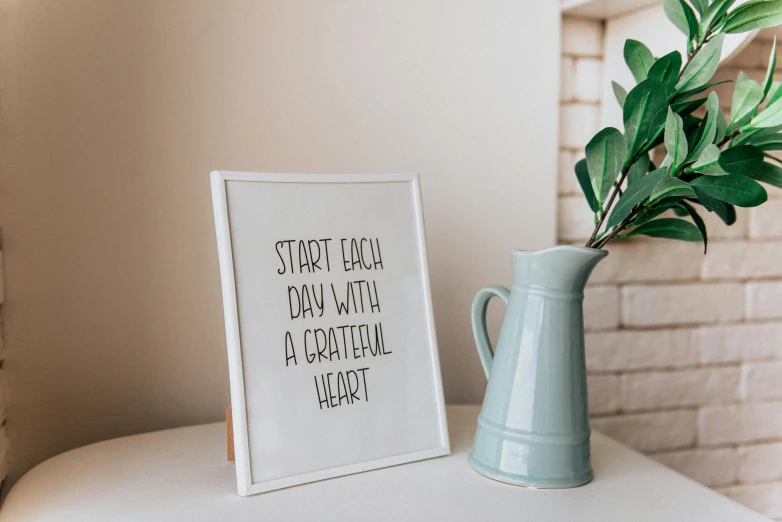 a picture frame sitting on top of a table next to a vase, unsplash, inspirational quote, start, made of all white ceramic tiles, heart