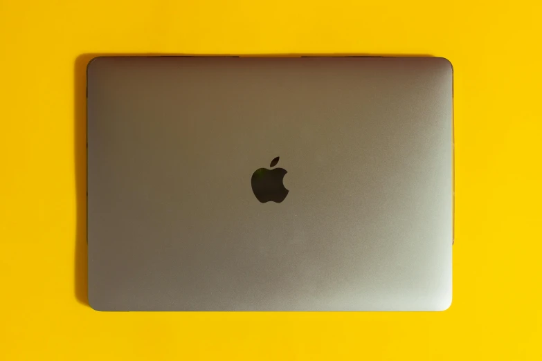 a laptop computer sitting on top of a yellow table, by Carey Morris, pexels, apple logo, lacquered, gradient brown to silver, black. yellow