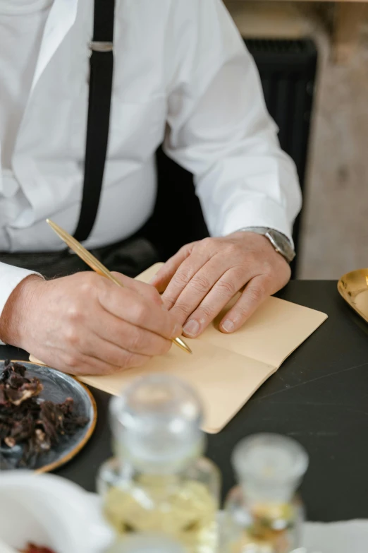 a man sitting at a table writing on a piece of paper, a still life, by Jessie Algie, unsplash, apothecary, gourmet and crafts, ignant, letters