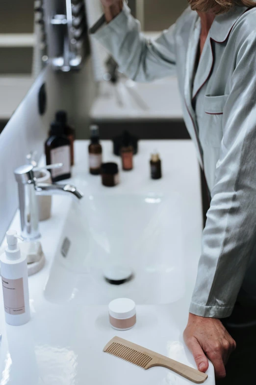 a woman brushing her hair in front of a mirror, pexels, wearing a labcoat, pink water in a large bath, hands on counter, reagents