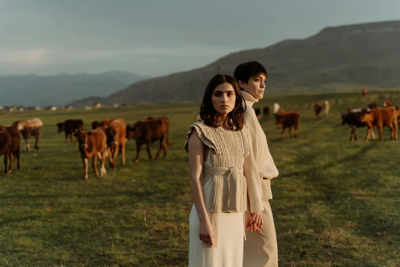 a man and a woman standing in front of a herd of cows, an album cover, by Emma Andijewska, pexels contest winner, renaissance, ayanamikodon and irakli nadar, hills in the background, fashion shoot, soft evening lighting