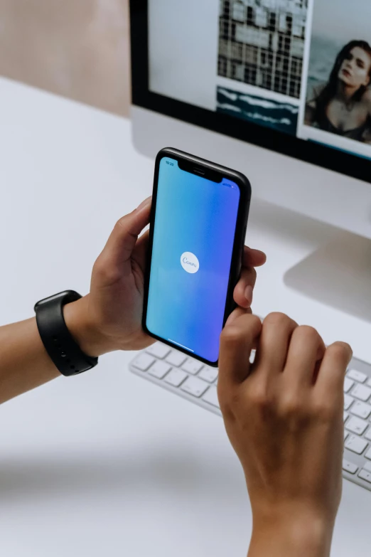 a person holding a phone in front of a computer, by Robbie Trevino, trending on pexels, holography, square, minimalist sticker, samsung smartthings, blue gradient