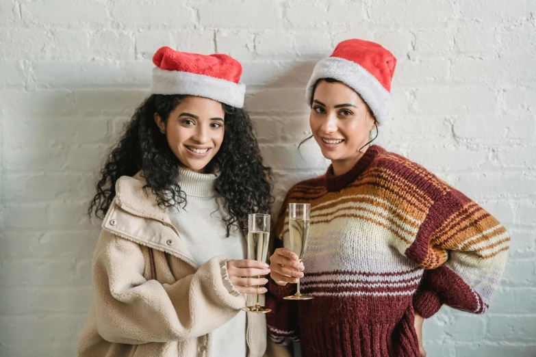 two women in santa hats holding glasses of champagne, pexels, imaan hammam, casual modern clothing, warm friendly expression, on a canva