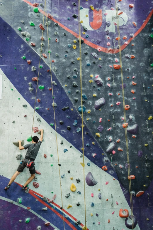 a man is climbing on a rock wall, trending on pexels, wide overhead shot, in the high school gym, nat geo, purple