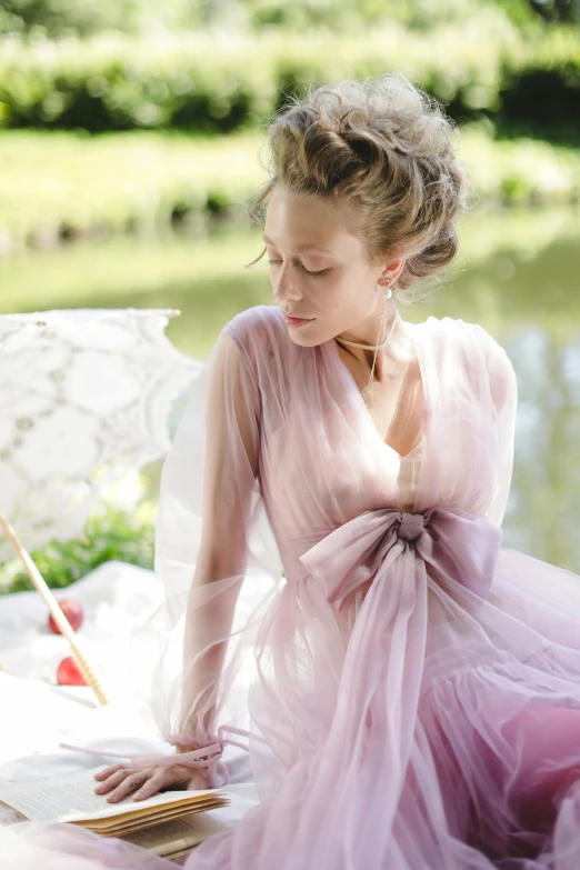 a woman in a pink dress sitting next to a body of water, wearing organza gown, al fresco, ethereal and dreamy theme, award-winning style