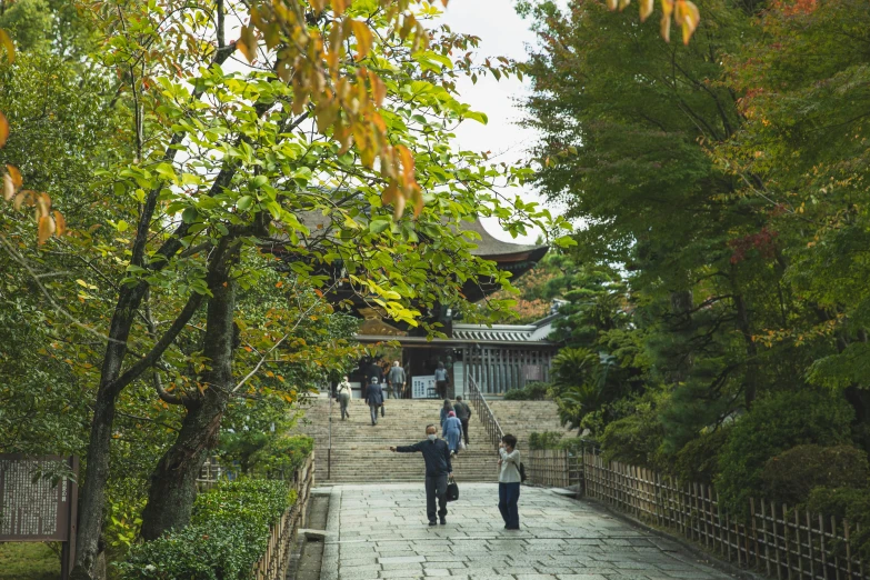 a couple of people that are walking down a path, shin hanga, temple in the distance, lots of foliage, steps, a wooden