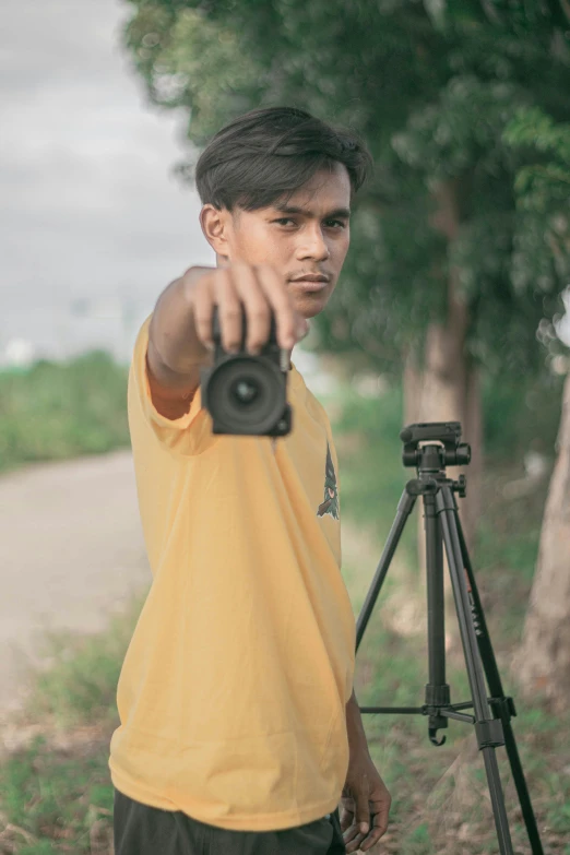 a man holding a camera on top of a tripod, by Basuki Abdullah, color video footage, looking directly at the camera, low quality footage, cinematic outfit photo