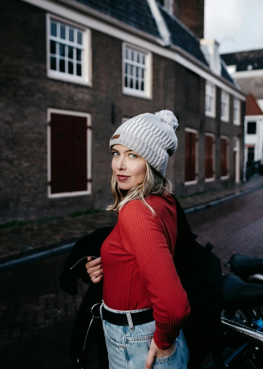 a woman standing next to a motorcycle on a street, inspired by Maud Naftel, pexels contest winner, beanie hat, netherlands, silver red white details, striped
