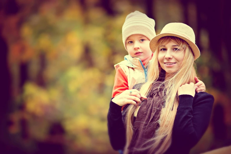 a woman holding a child in her arms, a photo, by Zofia Stryjenska, shutterstock, wearing a cute hat, square, fall, blonde