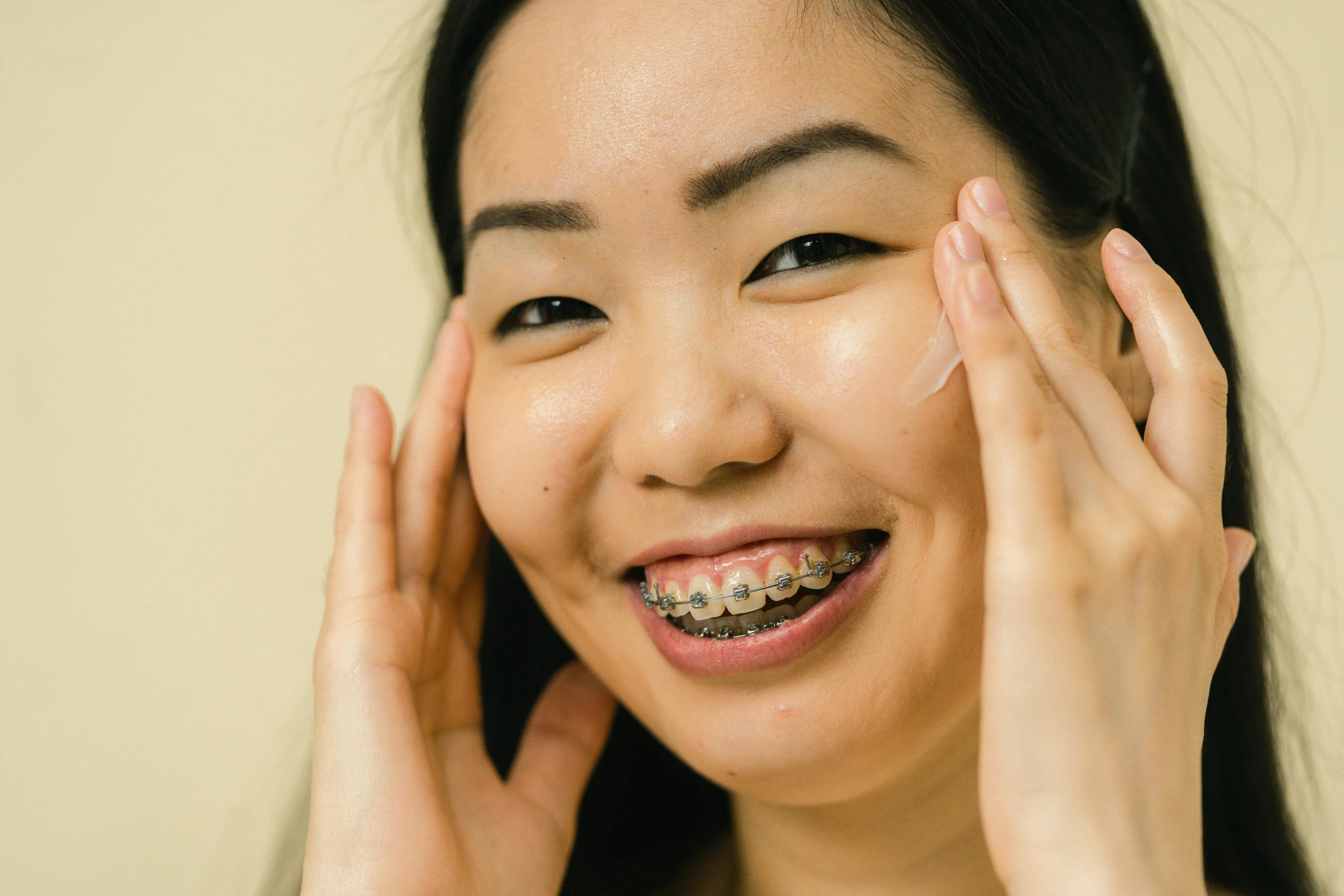 a close up of a person with braces on, a stipple, by Emma Andijewska, trending on pexels, mingei, asian face, creamy skin, smiling down from above, hands on face